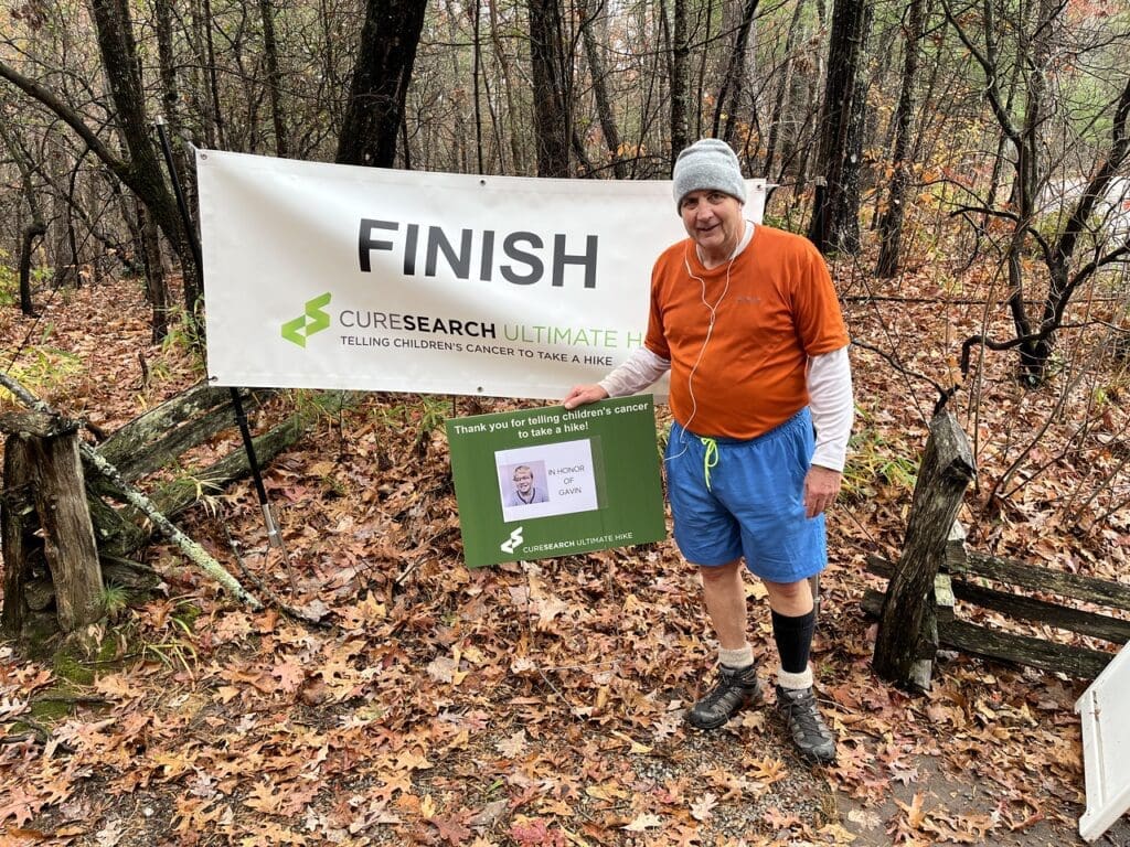 Frank Gioscia, Ultimate Hike's top fundraiser of all time, stands with a photo of childhood cancer survivor and family friend, Gavin, at the Foothills Fall Ultimate Hike finish line.